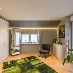 Modernes Schlafzimmer mit großem Kleiderschrank, Pflanzen und gemütlichem Sessel.