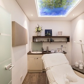 Moderner Behandlungsraum für Kosmetik mit Liege, Waschbecken und Naturmotiv an der Decke.