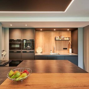 Moderne offene Küche mit Holzarbeitsplatte, dunklen Fronten und stilvoller Beleuchtung.